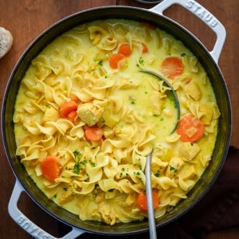 Pot of Ginger Turmeric Chicken Soup with a ladle in it on a wooden table.