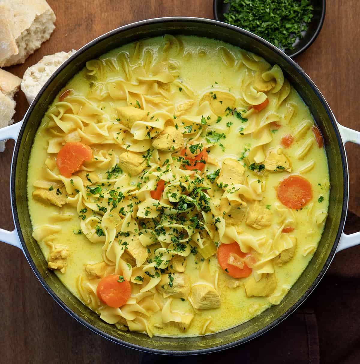 This Ginger Turmeric Chicken Soup is one of those recipes I make when I want something cozy and comforting. It’s a simple, golden soup with tender chicken, warm spices, and a creamy broth. Ginger and turmeric bring gentle warmth, and that beautiful color, and every spoonful feels soothing and nourishing! Pot of Ginger Turmeric Chicken Soup on a wooden table from overhead.