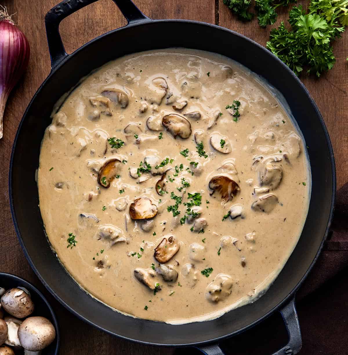 This Mushroom Shallot Gravy is easy, flavorful, and perfect for drizzling over roasted meats, mashed potatoes, or biscuits! Skillet of Mushroom Shallot Gravy on a wooden table with baby bella's and a shallot.