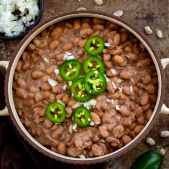 Bowl of Pinto Beans on a table with fresh cut onions and jalapeno slices.