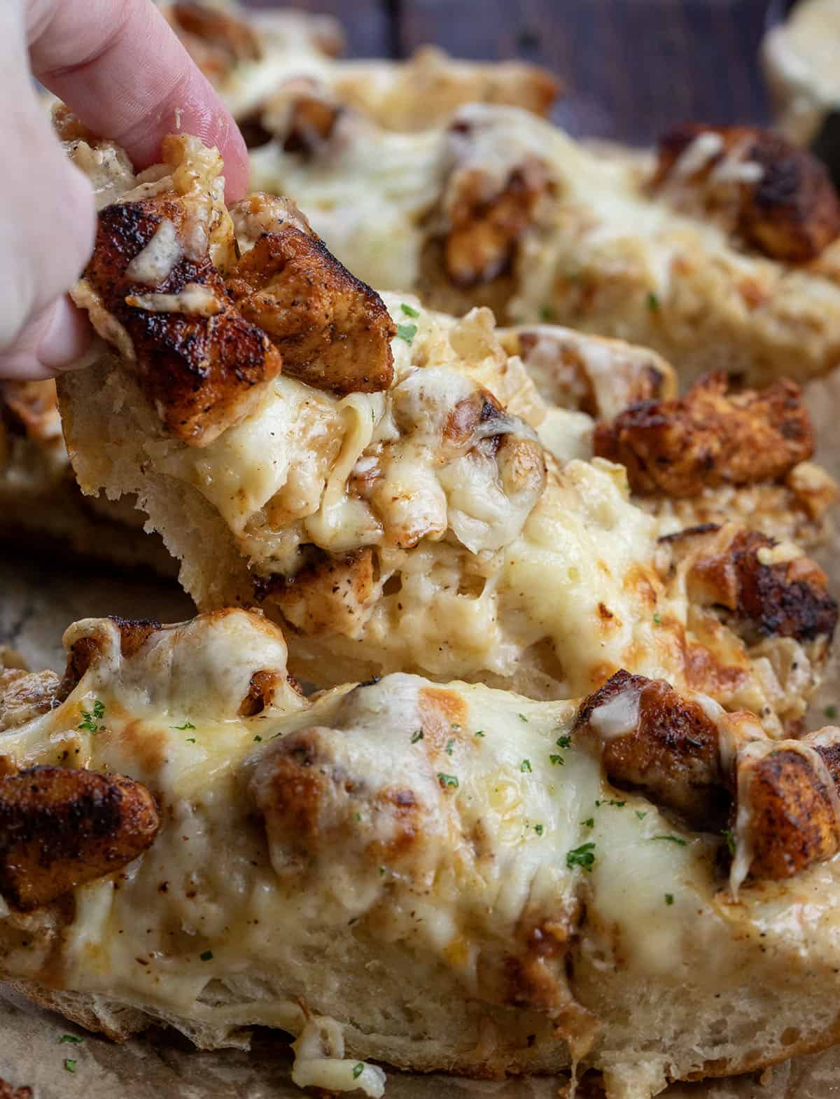 Very close up of hand picking up a slice of Blackened Chicken Alfredo Garlic Bread.
