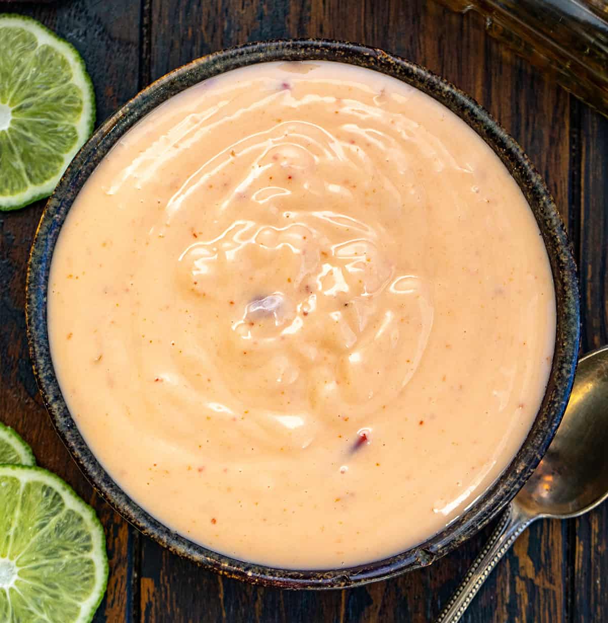 Creamy, sweet, spicy, and just a little boozy, this Bourbon Bang Bang Sauce is everything you love about Bang Bang sauce with a caramel-forward twist. Drizzle it over chicken, shrimp, roasted veggies, or use it as a dip for fries. Quick to whip up and totally addictive! Black bowl filled with Bourbon Bang Bang Sauce on a wooden table.