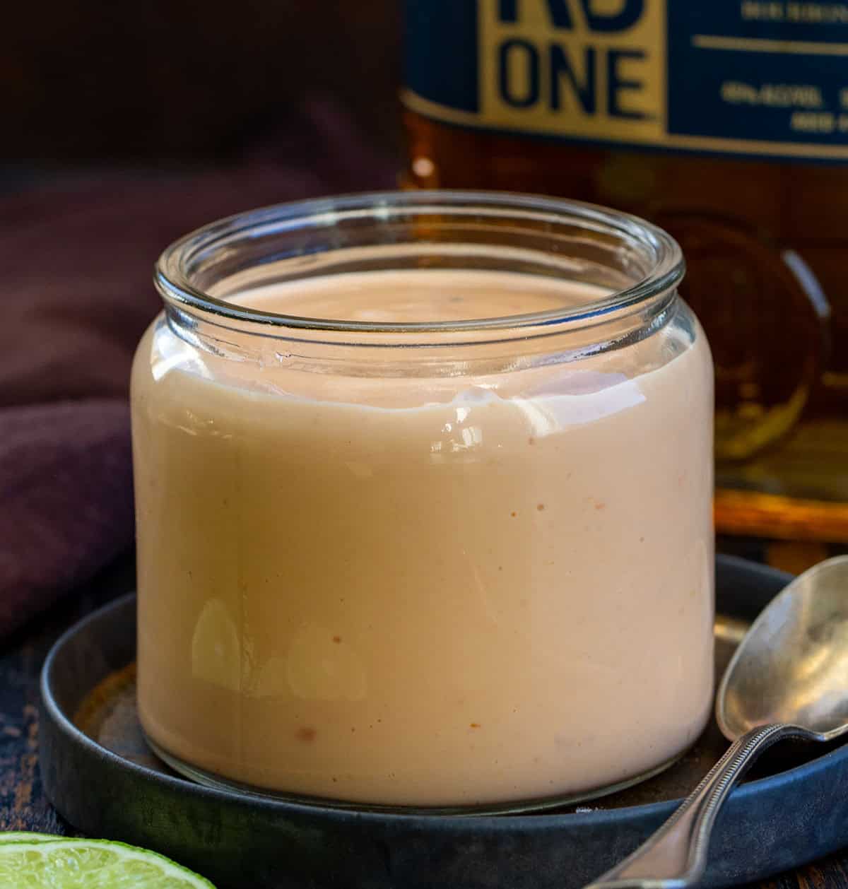 Creamy, sweet, spicy, and just a little boozy, this Bourbon Bang Bang Sauce is everything you love about Bang Bang sauce with a caramel-forward twist. Drizzle it over chicken, shrimp, roasted veggies, or use it as a dip for fries. Quick to whip up and totally addictive! Jar of Bourbon Bang Bang Sauce in front of a bourbon bottle.