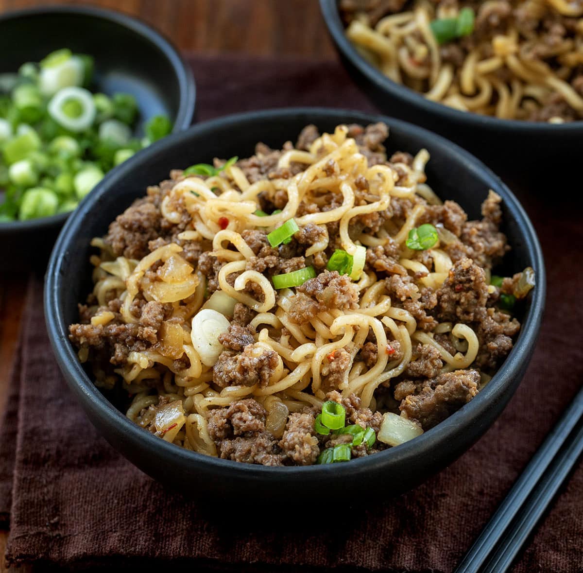 Chili Beef Garlic Noodles are a fast, flavor-packed weeknight dinner that tastes like takeout garlic noodles with a hearty beef twist. It’s cozy, balanced, and surprisingly easy to pull off on a busy night; it's ready in under 30 minutes! Black bowls of Chili Beef Garlic Noodles on a wooden table.