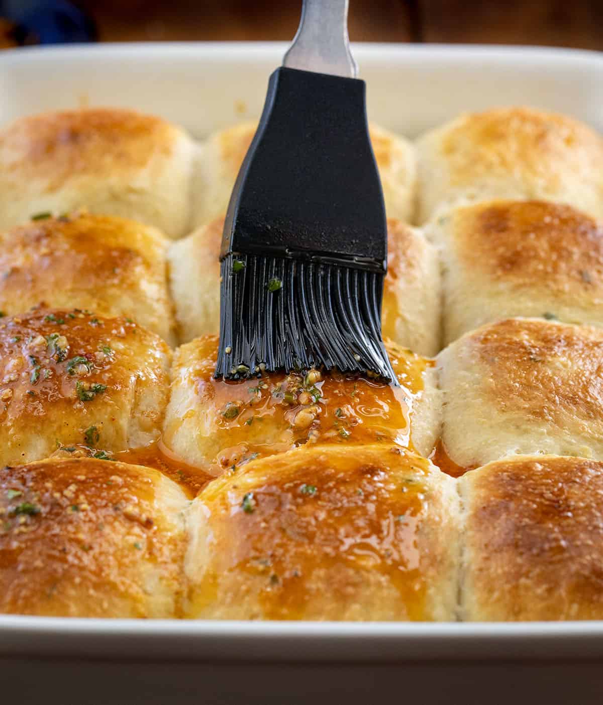 These Cowboy Butter Dinner Rolls are soft, fluffy, and brushed with my homemade cowboy butter. Pull them apart straight from the pan... you won’t be able to stop at just one! Brushing cowboy butter onto herb dinner rolls.