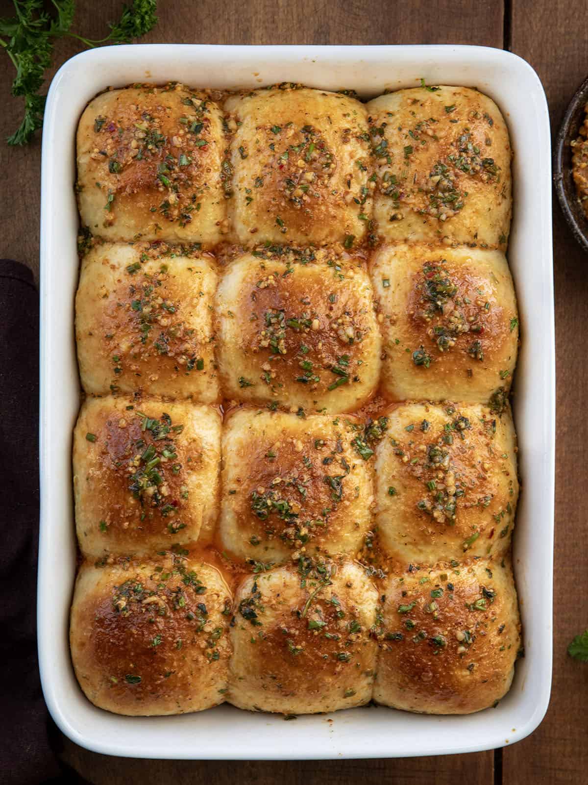 These Cowboy Butter Dinner Rolls are soft, fluffy, and brushed with my homemade cowboy butter. Pull them apart straight from the pan... you won’t be able to stop at just one! Pan of Cowboy Butter Dinner Rolls on a wooden table from overhead.