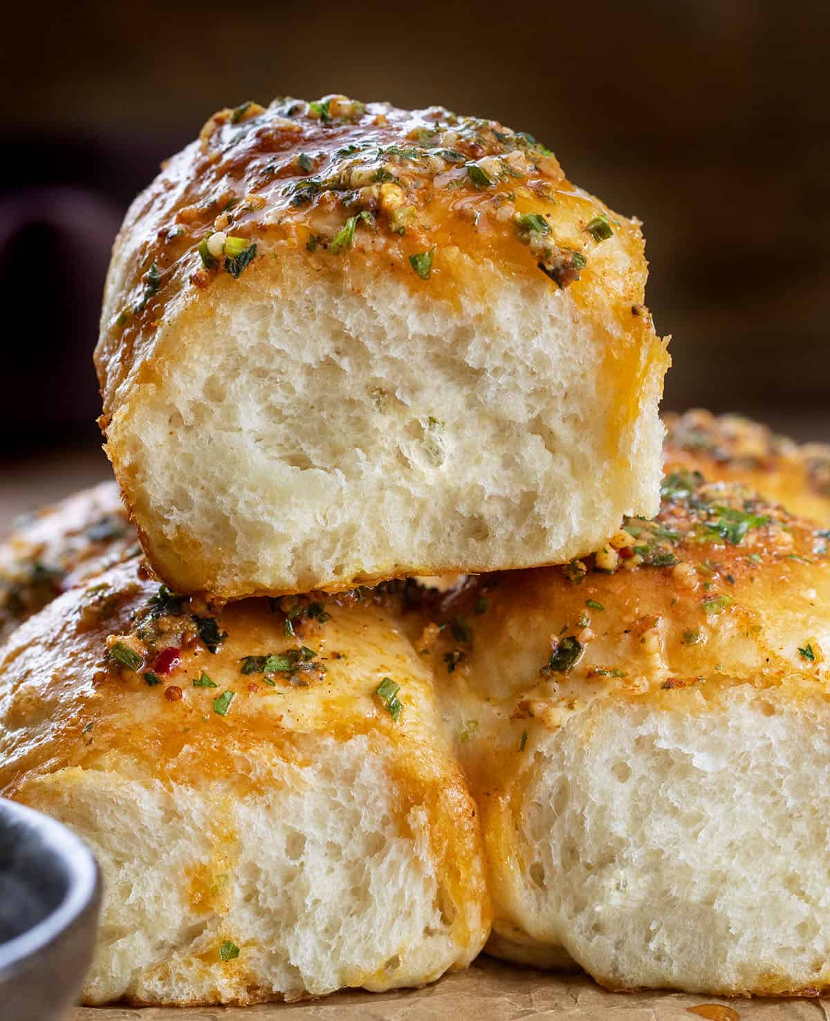 These Cowboy Butter Dinner Rolls are soft, fluffy, and brushed with my homemade cowboy butter. Pull them apart straight from the pan... you won’t be able to stop at just one! Stack of Cowboy Butter Dinner Rolls on a wooden table.