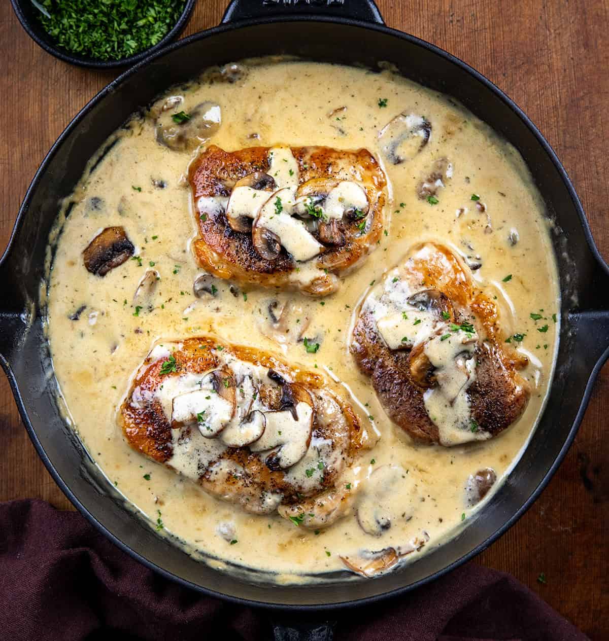 Creamy Ranch and Mushroom Pork Chops are seared until golden, then simmered in a rich ranch cream sauce with tender mushrooms and Parmesan. Skillet of Creamy Ranch and Mushroom Pork Chops on a wooden table from overhead.