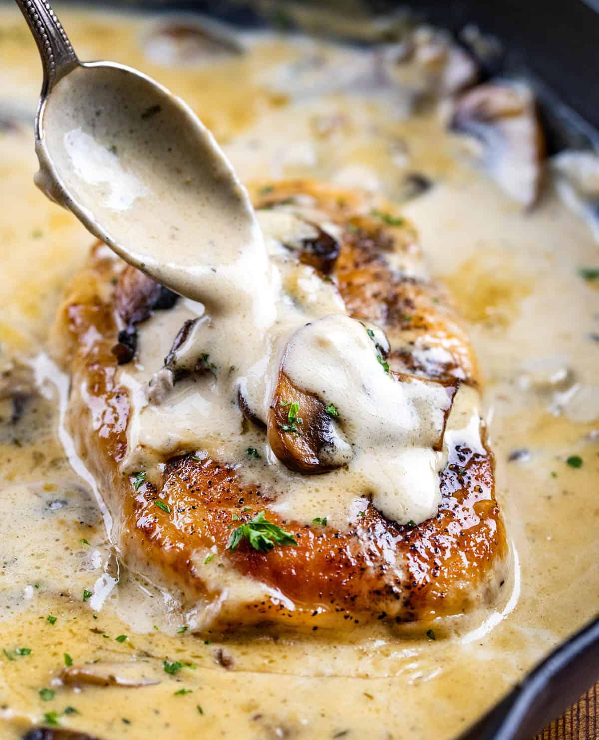 Creamy Ranch and Mushroom Pork Chops are seared until golden, then simmered in a rich ranch cream sauce with tender mushrooms and Parmesan. Spooning sauce over a pork chop with mushrooms.