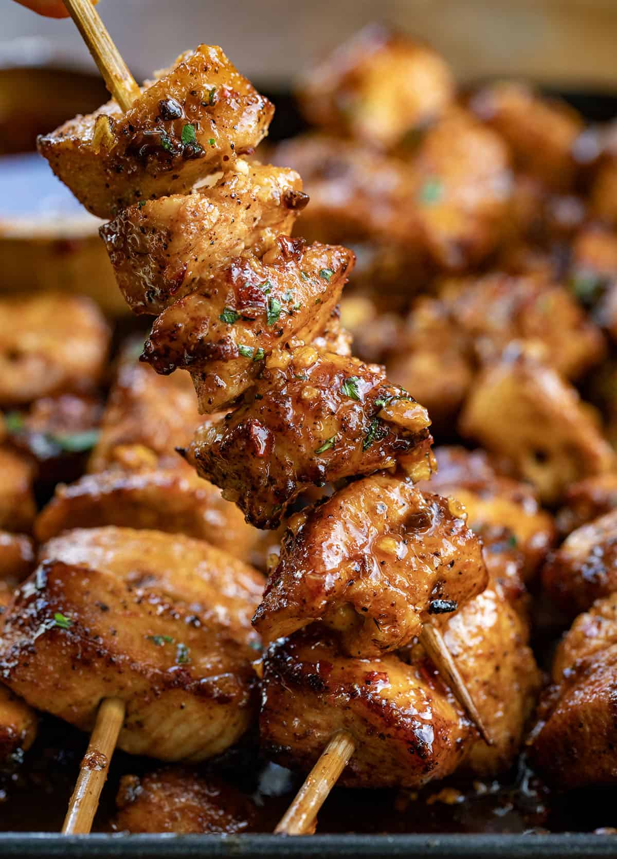 These Garlic Chili Chicken Skewers are juicy, flavorful, and packed with a sweet-and-spicy kick! Hand holding one Garlic Chili Chicken Skewer.