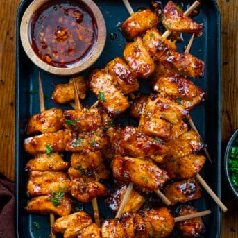 Black pan filled with Garlic Chili Chicken Skewers and garlic chili oil.