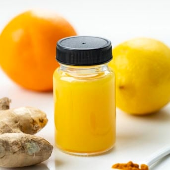 Jars of Ginger Shots with orange, lemon, turmeric, and ginger near the bottles.