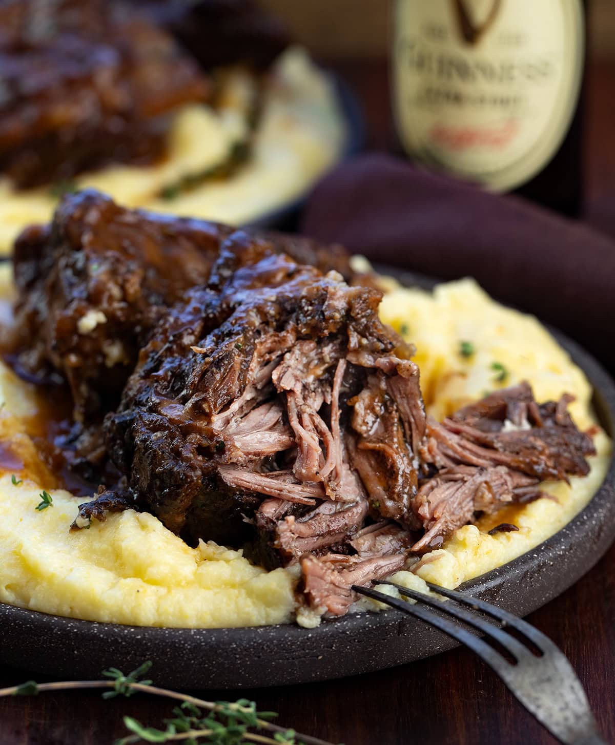 Rich, savory, and slow-braised to perfection, these ribs are cooked in bold Guinness stout, fresh herbs, and a luscious beef broth. The silky pan sauce is perfect spooned over mashed potatoes or noodles, all in one pot for easy, impressive comfort food. Close up of tender, falling apart Guinness Short Ribs on polenta.