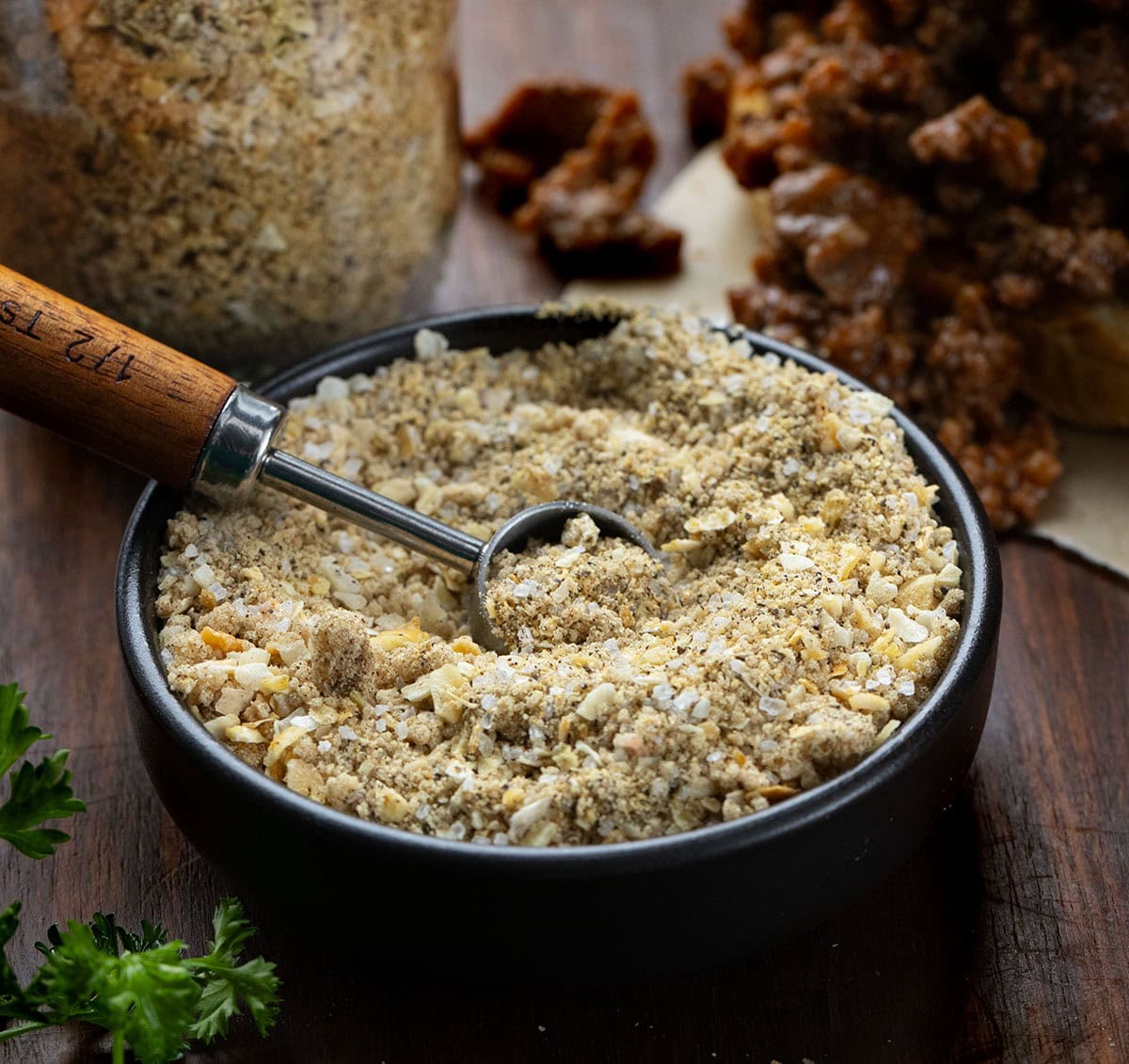 Homemade Sloppy Joe Dry Mix is a simple, pantry-friendly mix that you can whip up in minutes and keep on hand for months. Just a few tablespoons of this mix and ground beef turns into rich, savory, slightly sweet Sloppy Joes that everyone will love! Dish of Homemade Sloppy Joe Dry Mix on a wooden table with a jar filled with Homemade Sloppy Joe Dry Mix and a sloppy joe sandwich.