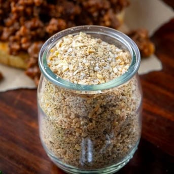 Jar of Homemade Sloppy Joe Dry Mix on a wooden table in front of a sloppy joe sandwich.