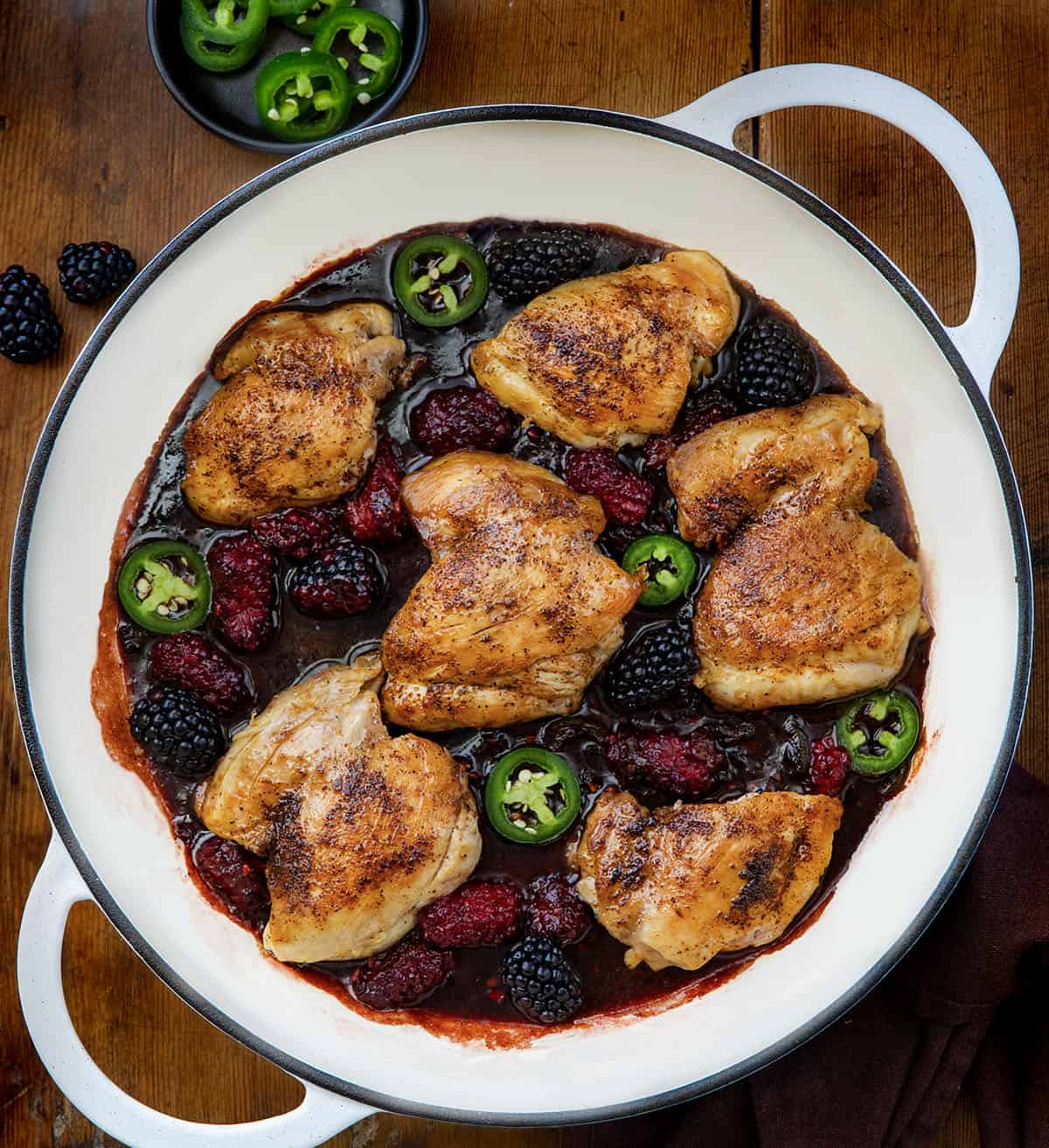 Skillet of Jalapeño Blackberry Chicken on a wooden table from overhead.