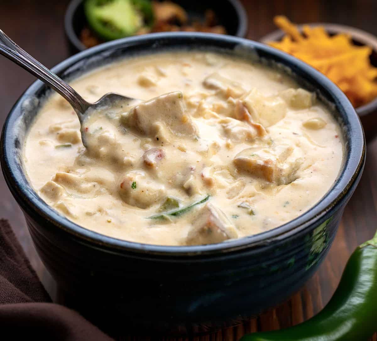Creamy, cheesy, and just the right amount of spice! This Jalapeño Popper Chicken Soup is packed with tender chicken, crispy bacon, gooey cheese, and a kick of jalapeño. Perfect for cozy nights, weeknight dinners, or anytime you want a comforting, hearty bowl of deliciousness. Bowl of Jalapeño Popper Chicken Soup with a spoon int he process of taking a bite.