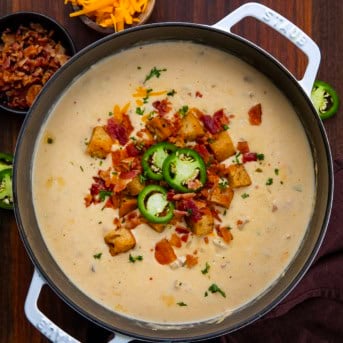 Pot filled with Jalapeño Popper Chicken Soup garnished with bacon bits and fresh slices of jalapeno and homemade croutons from overhead.