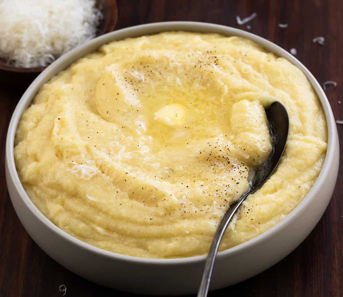 Creamy polenta is comfort food made simple. Slowly cooked fine cornmeal turns buttery and smooth, creating the perfect base for hearty meals or cozy weeknight dinners! Bowl of Creamy Polenta on a wooden table with a spoon.