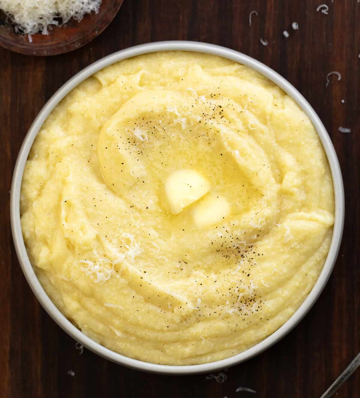 Creamy polenta is comfort food made simple. Slowly cooked fine cornmeal turns buttery and smooth, creating the perfect base for hearty meals or cozy weeknight dinners! Bowl of Creamy Polenta on a wooden table from overhead.