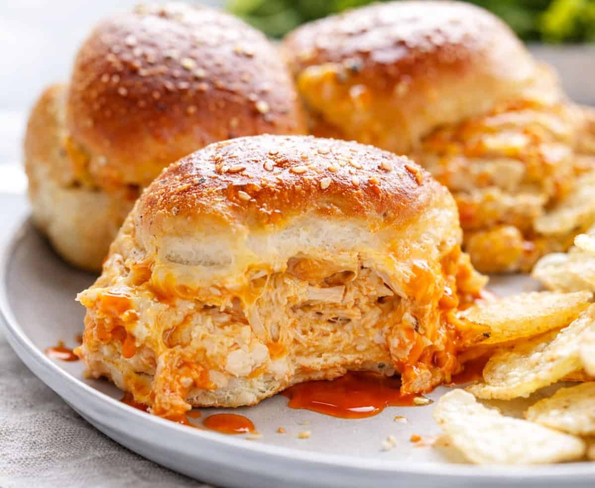 Sliders are one of the easiest ways to feed a crowd. They’re fun, customizable, and perfect for parties, game days, holidays, and family dinners! Close up of Buffalo Chicken Sliders on a white plate with buffalo sauce.
