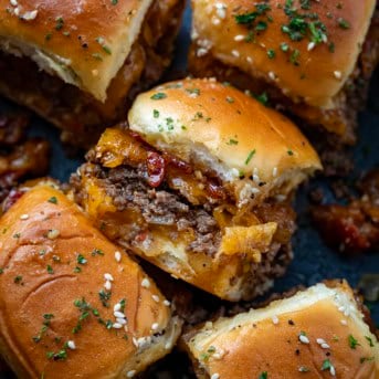 Close up of Bacon Jam Cheeseburger Sliders in a black pan with one slider tipped over on its side.