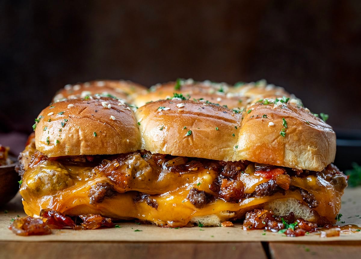 These Bacon Jam Cheeseburger Sliders are soft, sweet Hawaiian rolls layered with juicy, seasoned ground beef, melty cheddar, and smoky homemade bacon jam. Side view of Bacon Jam Cheeseburger Sliders showing the melty cheese and bacon jam in detail.