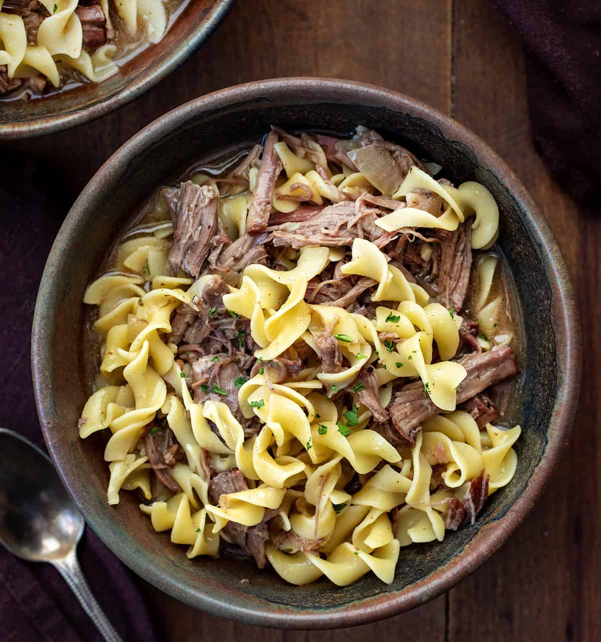 This Slow Cooker Beef and Noodles is a cozy, family-friendly dinner with tender, fall-apart beef, rich savory gravy, and soft egg noodles. Easy to make and perfect for busy weeknights or a comforting weekend meal. Bowls of Beef and Noodles on a wooden table from overhead.