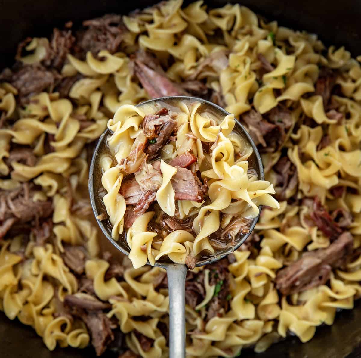 This Slow Cooker Beef and Noodles is a cozy, family-friendly dinner with tender, fall-apart beef, rich savory gravy, and soft egg noodles. Easy to make and perfect for busy weeknights or a comforting weekend meal. Ladle full of Beef and Noodles held over the crockpot.