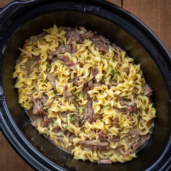 Crockpot of Beef and Noodles on a wooden table.
