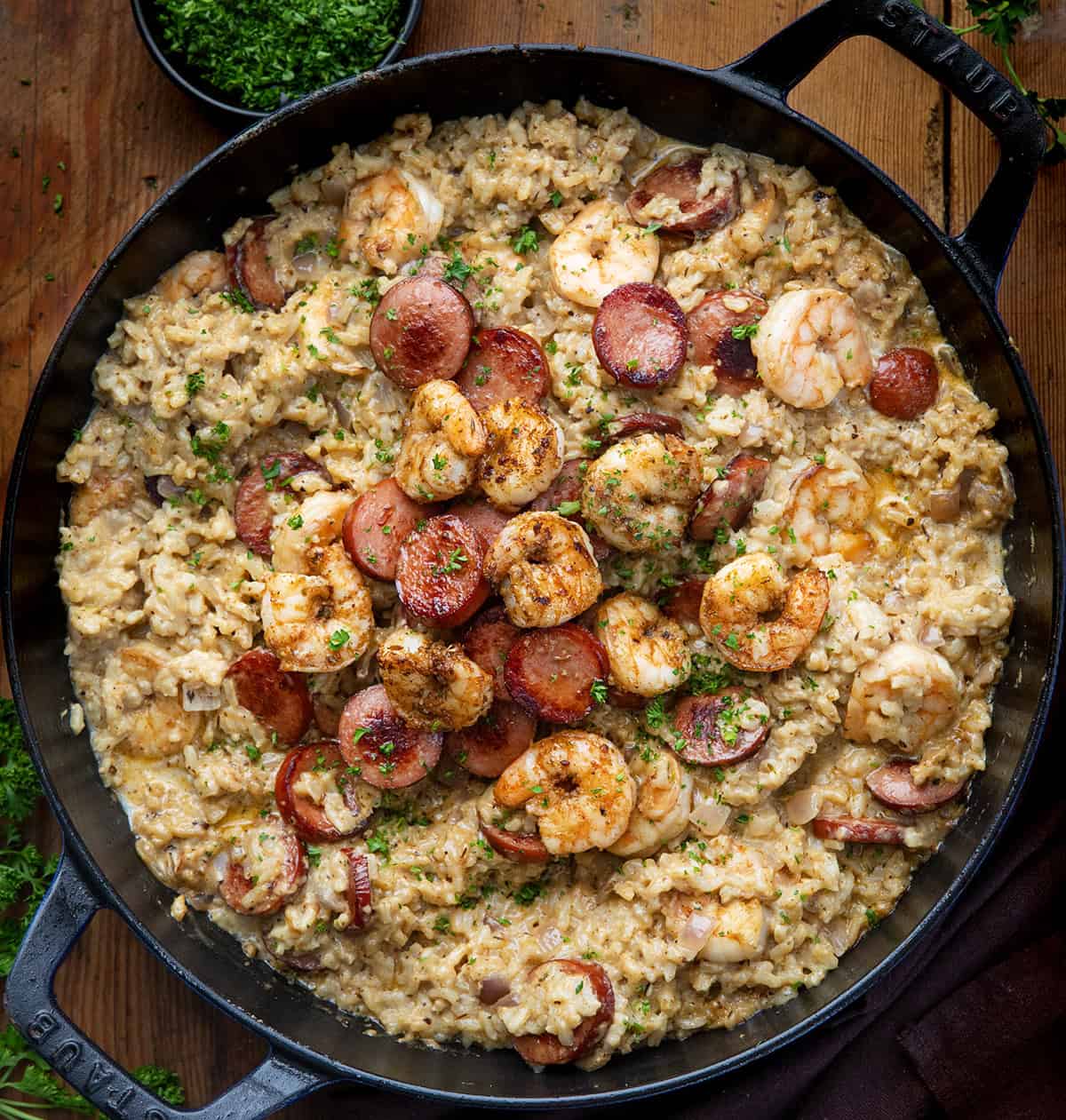 This Cajun Shrimp and Sausage Rice is packed with bold, smoky flavors. Tender shrimp, crispy sausage, and perfectly seasoned rice are tossed in a creamy Cajun sauce for a hearty, family-friendly meal. Black skillet of Cajun Shrimp and Sausage Rice on a wooden table from overhead.