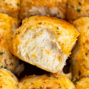 CLose up of one Cheesy Cowboy Butter Dinner Roll on its side next to other rolls.