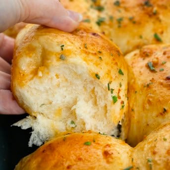 Hand picking up a Cheesy Cowboy Butter Dinner Roll from the pan.