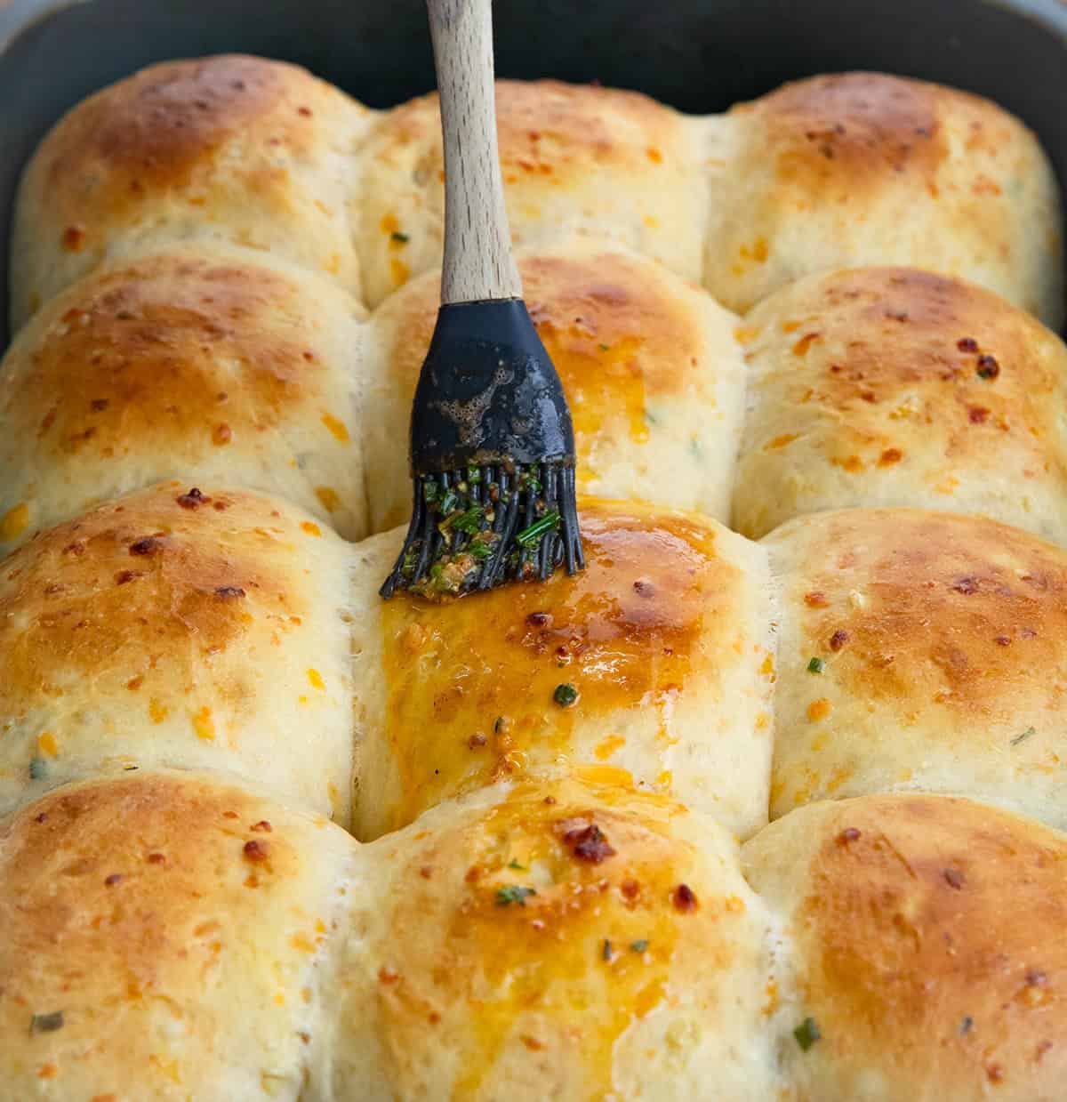 These Cheesy Cowboy Butter Dinner Rolls are the best of both worlds: a mash-up of my Cheesy Garlic Dinner Rolls and my popular Cowboy Butter Dinner Rolls (without cheese), both of which are amazing on their own! Brushing Cowboy Butter over Cheesy Cowboy Butter Dinner Rolls.