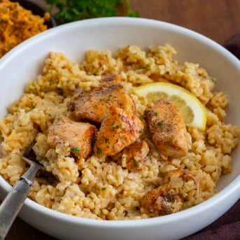 White bowl of Cowboy Butter Chicken and Rice on a wooden table with a fork.
