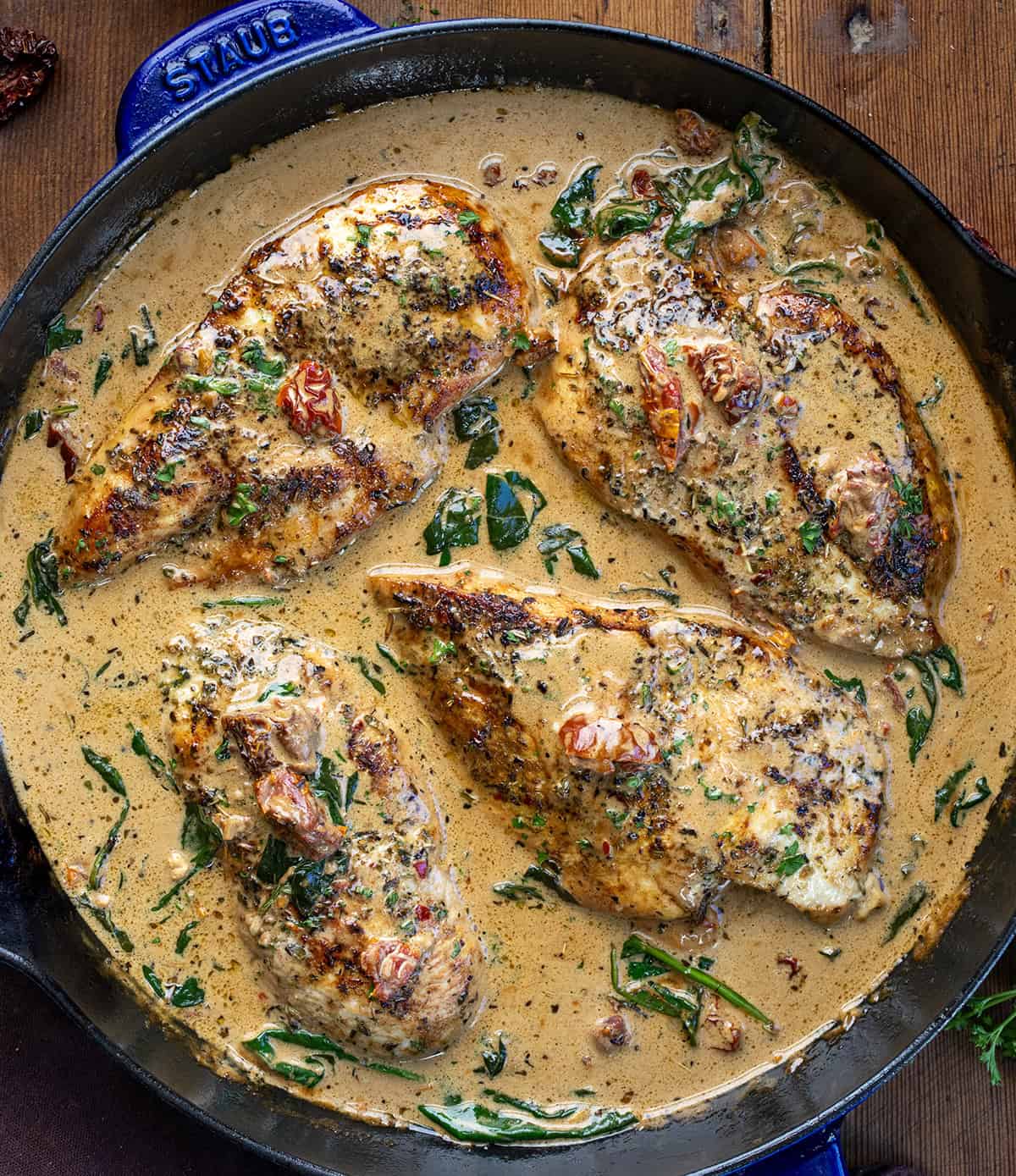Tender chicken breasts simmered in a rich, creamy Tuscan sauce with sun-dried tomatoes, spinach, and Parmesan cheese! Creamy Tuscan Chicken with Homemade Tuscan Seasoning in a skillet on a wooden table from overhead.