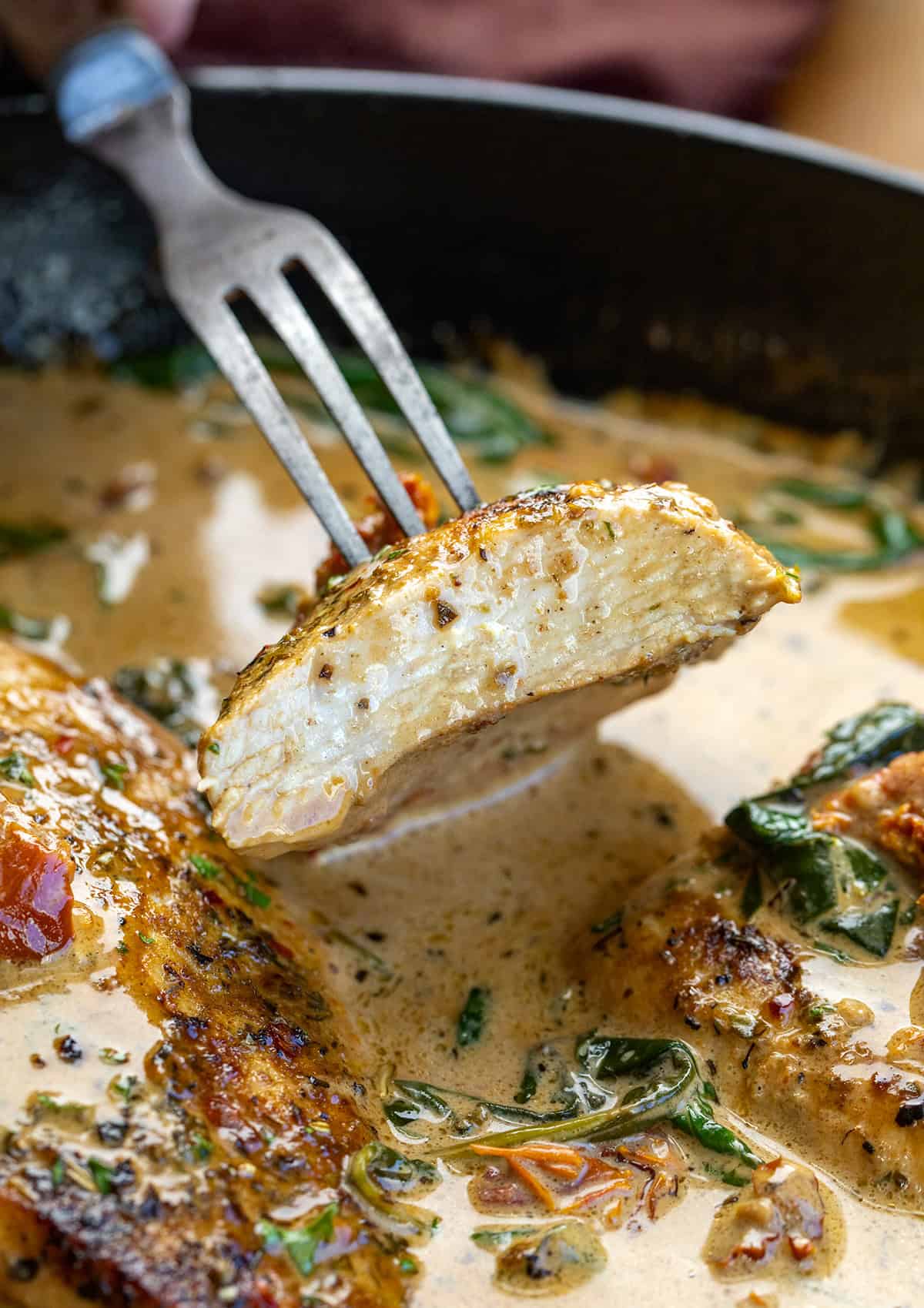 Tender chicken breasts simmered in a rich, creamy Tuscan sauce with sun-dried tomatoes, spinach, and Parmesan cheese! Fork holding a piece of Creamy Tuscan Chicken.