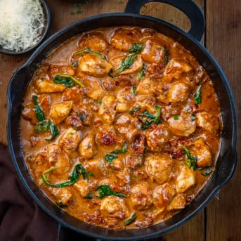 Skillet of Creamy Tuscan Chicken Bites on a wooden table from overhead.