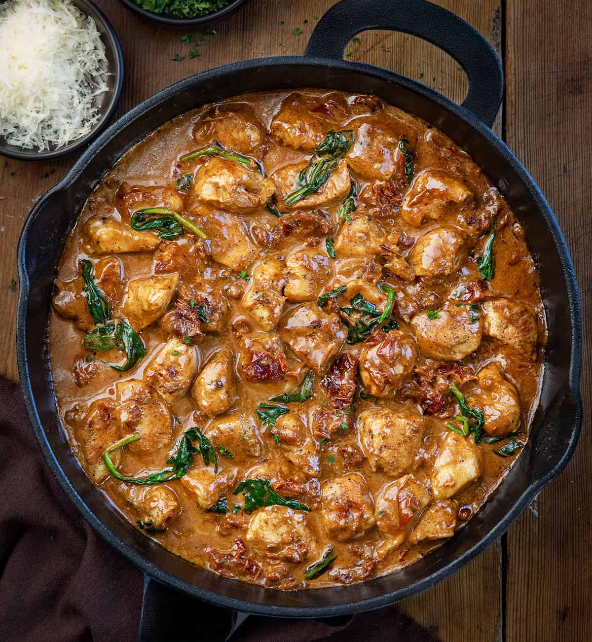 Tender chicken bites cooked in a rich, creamy sauce with sun-dried tomatoes, spinach, Parmesan, and a hint of garlic! Skillet of Creamy Tuscan Chicken Bites on a wooden table from overhead.