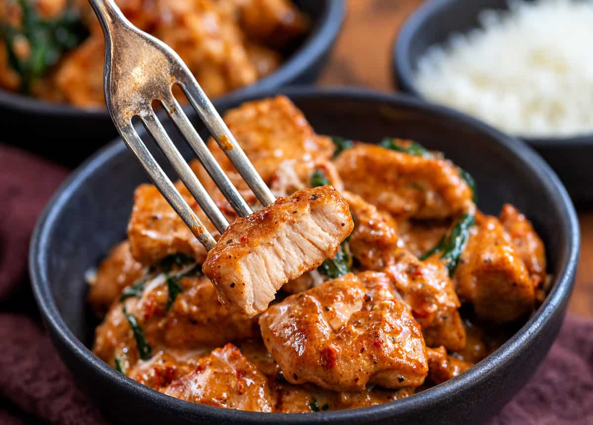 Tender chicken bites cooked in a rich, creamy sauce with sun-dried tomatoes, spinach, Parmesan, and a hint of garlic! Fork with a Creamy Tuscan Chicken Bite on it that has been bitten into.