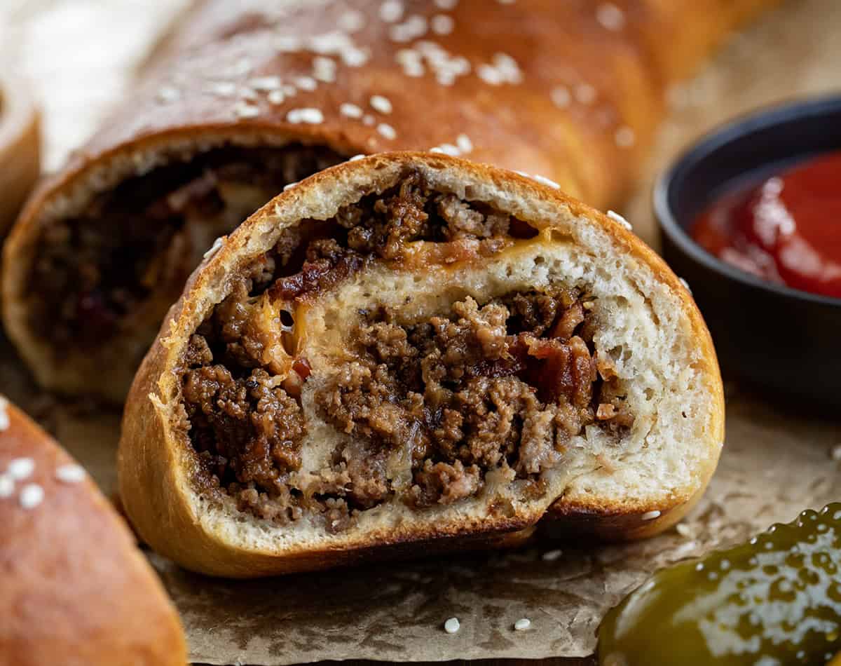 Bacon Cheeseburger Garbage Bread is packed with seasoned beef, crispy bacon, and melted cheddar, all rolled up in golden dough. Slice and serve warm with your favorite dipping sauces for a fun family dinner or game-day snack! Slice of Garbage Bread cut from loaf very close up.