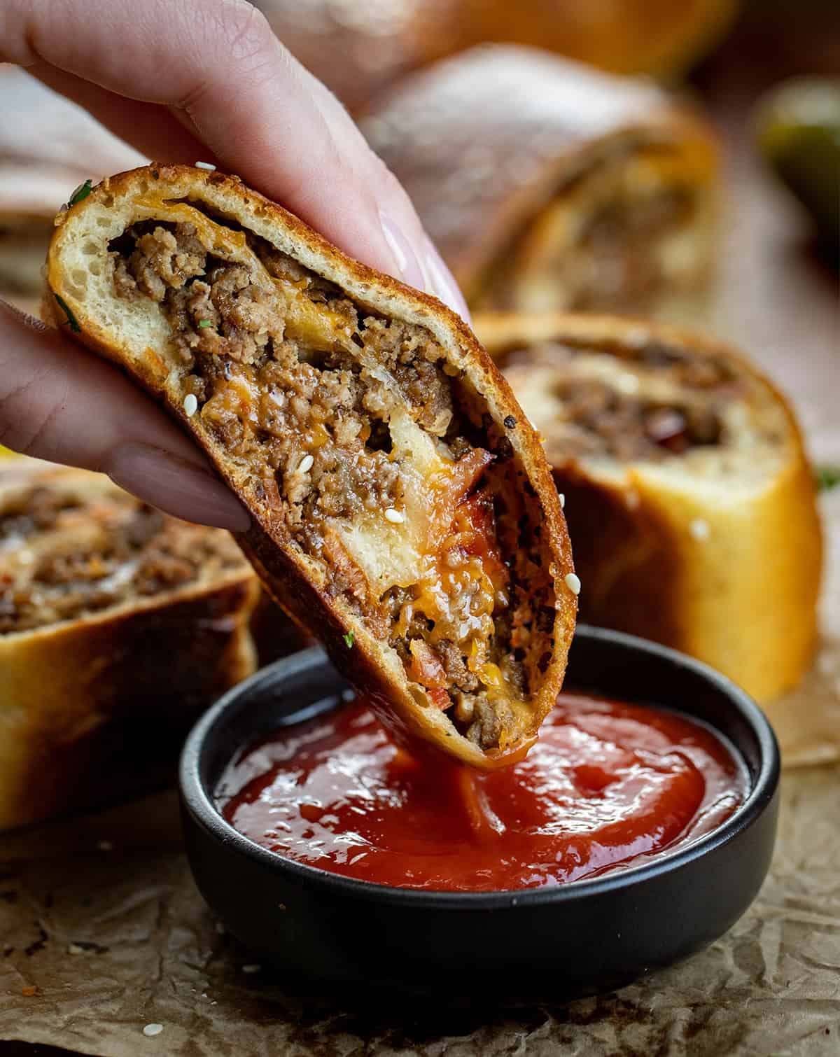 Bacon Cheeseburger Garbage Bread is packed with seasoned beef, crispy bacon, and melted cheddar, all rolled up in golden dough. Slice and serve warm with your favorite dipping sauces for a fun family dinner or game-day snack! Dipping garbage bread into ketchup.