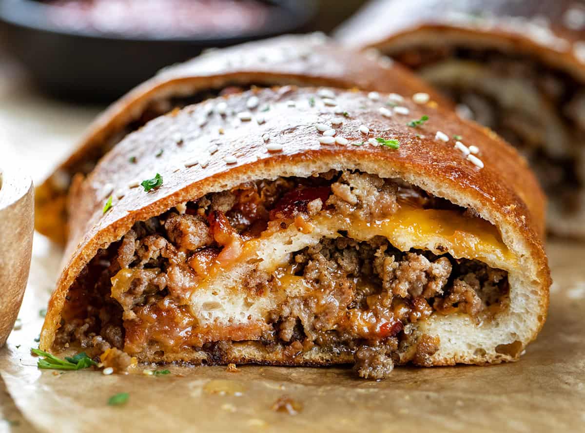 Bacon Cheeseburger Garbage Bread is packed with seasoned beef, crispy bacon, and melted cheddar, all rolled up in golden dough. Slice and serve warm with your favorite dipping sauces for a fun family dinner or game-day snack! Close up of slice of Garbage Bread.