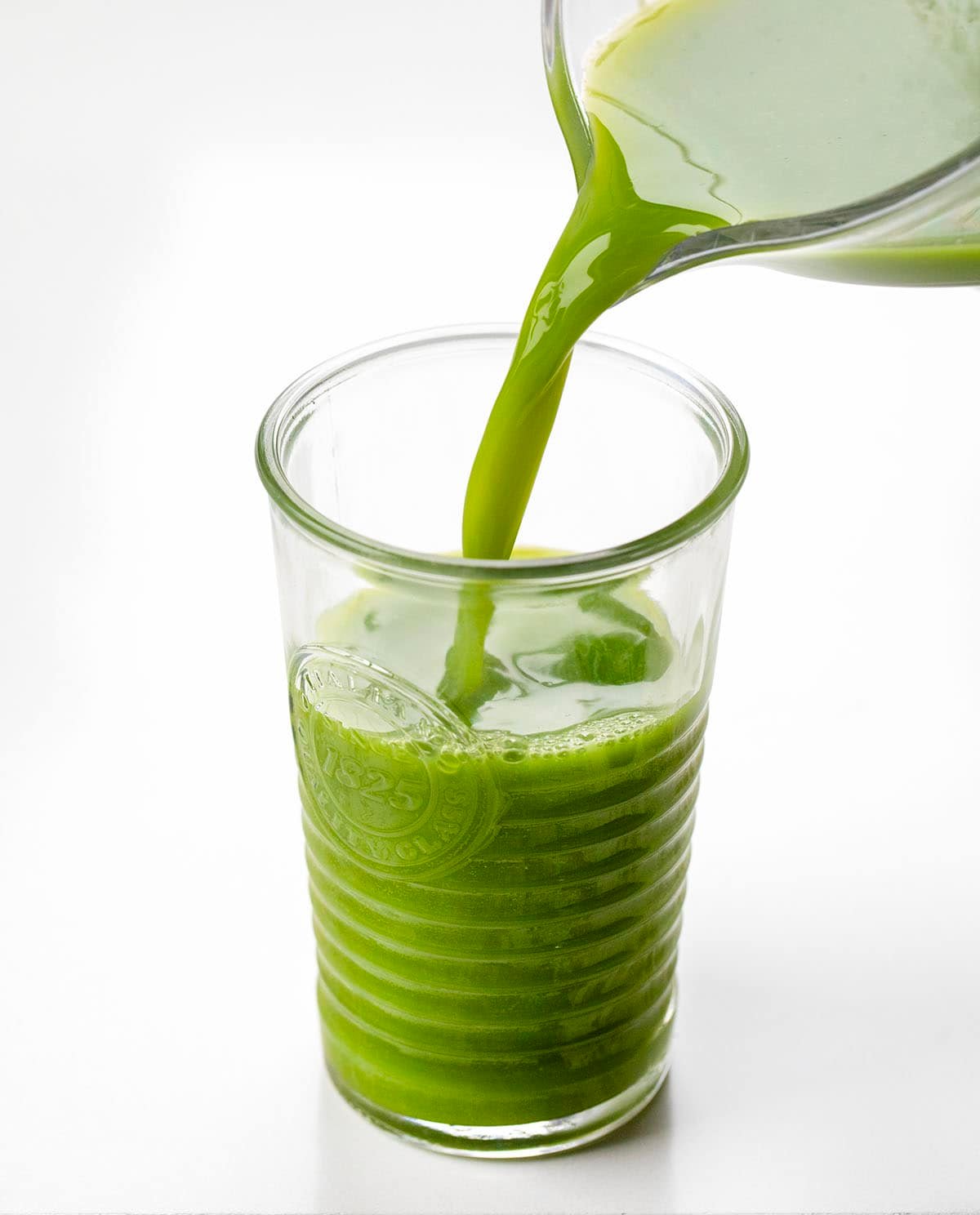 Keep your wellness routine fresh and bright with this Greens Immunity Booster! Made with crisp apples, leafy greens, zesty lemon, and a little spicy ginger, these shots are a simple, refreshing way to add a little natural energy to your day! Pouring Greens Immunity Booster into a glass.