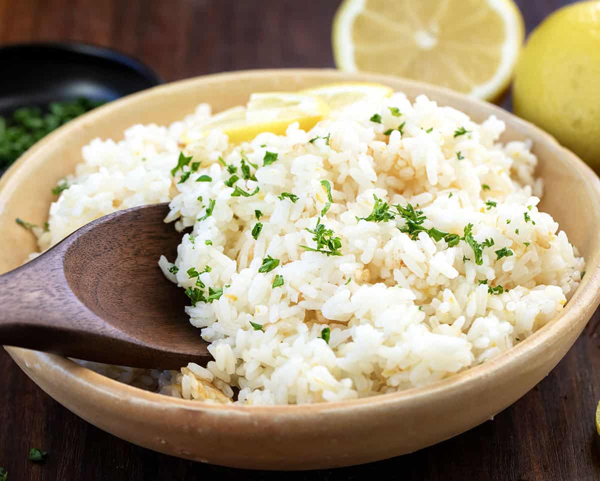 Elevate your meals with Lemon Rice, a flavorful side dish made with fresh lemon juice and butter for perfect tenderness! Bowl of Lemon Rice with a wooden spoon in it.