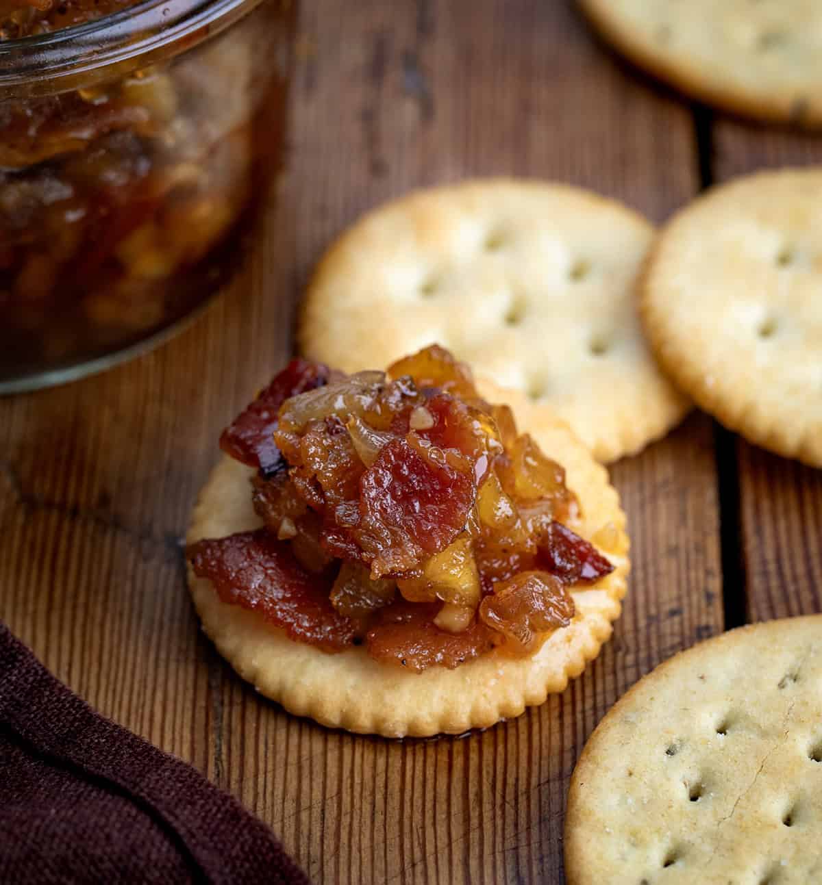 Sweet, smoky, and a little bit tropical, this Pineapple Bacon Jam is a flavor-packed topping for toast, burgers, or roasted veggies. Crispy bacon, juicy pineapple, and a touch of spice make it irresistibly addictive! Cracker with Pineapple Bacon Jam on it on a wooden table.