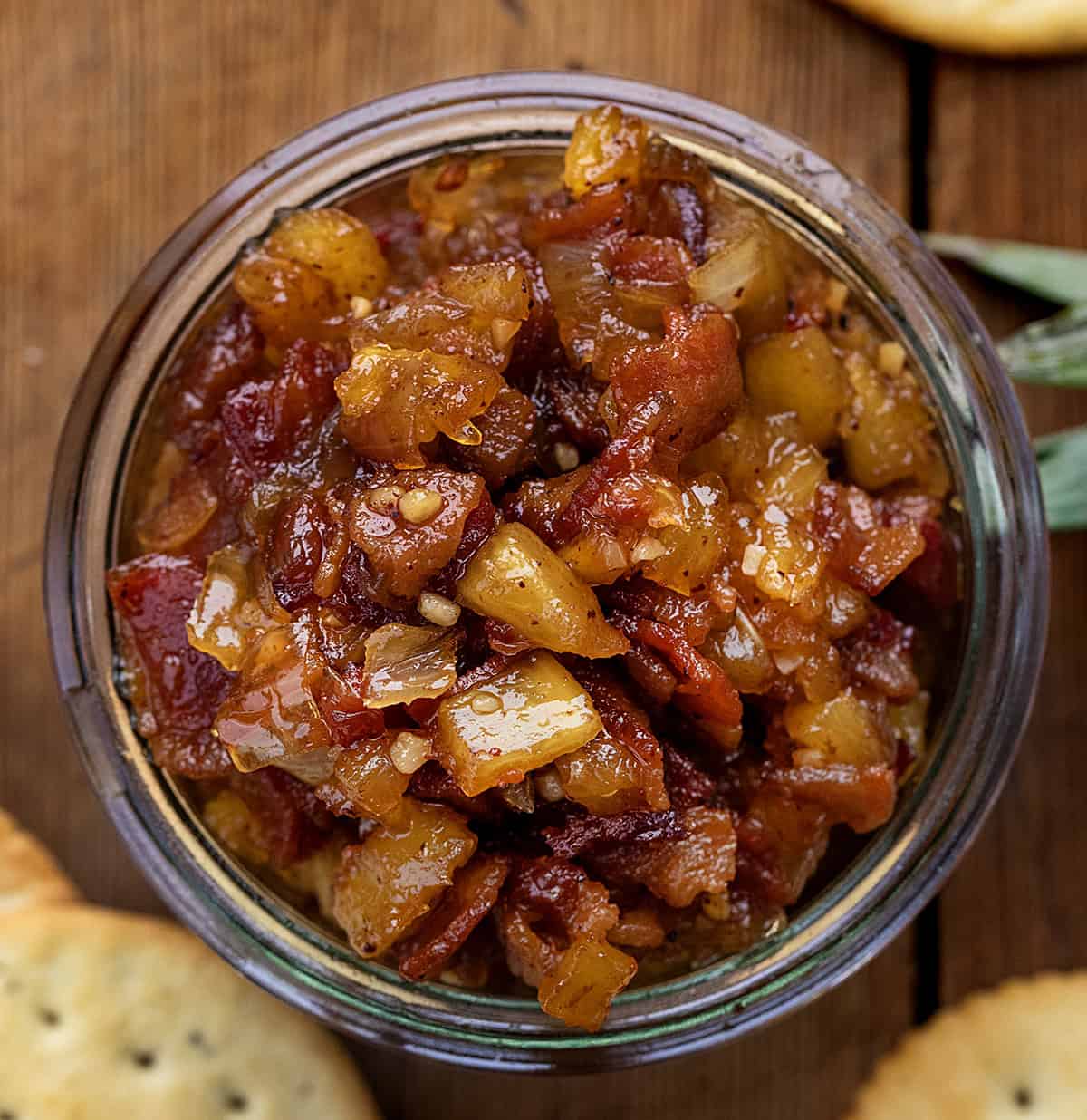 Sweet, smoky, and a little bit tropical, this Pineapple Bacon Jam is a flavor-packed topping for toast, burgers, or roasted veggies. Crispy bacon, juicy pineapple, and a touch of spice make it irresistibly addictive! Looking down on a jar of Pineapple Bacon Jam on a wooden table.
