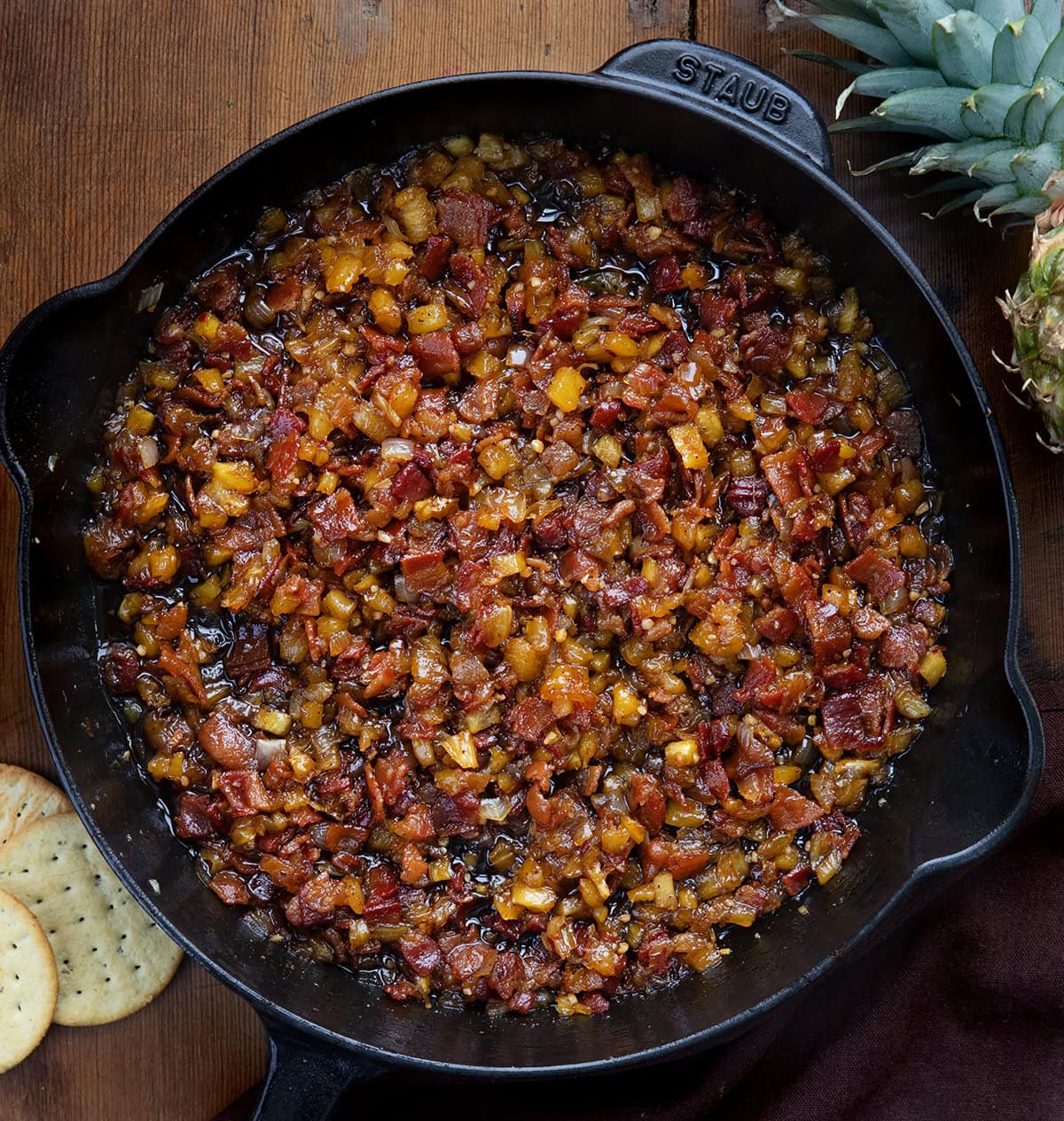 Sweet, smoky, and a little bit tropical, this Pineapple Bacon Jam is a flavor-packed topping for toast, burgers, or roasted veggies. Crispy bacon, juicy pineapple, and a touch of spice make it irresistibly addictive! Black skillet of Pineapple Bacon Jam on a wooden table from overhead.