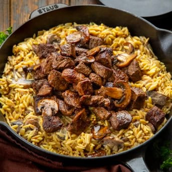 Skillet of Steak Bites with Creamy Mushroom Orzo on a wooden table.