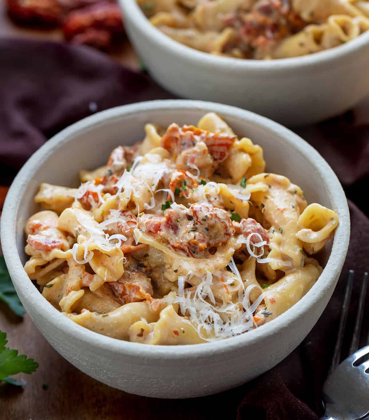 Creamy Sun-Dried Tomato Pasta is a quick and flavorful pasta with sun-dried tomatoes, garlic, Parmesan, and Tuscan seasoning. Ready in under 30 minutes, this comforting dish is perfect for weeknight dinners. Close up of a bowl of Sun-Dried Tomato Pasta on a wooden table.